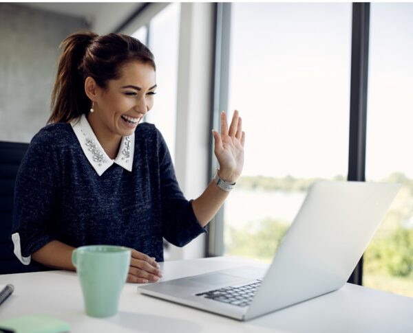 Happy businesswoman using laptop and having fun while greeting someone during a video call in the office.